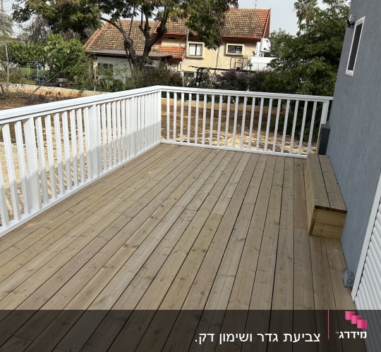 מרפסת עץ עם מעקה לבן ליד בית